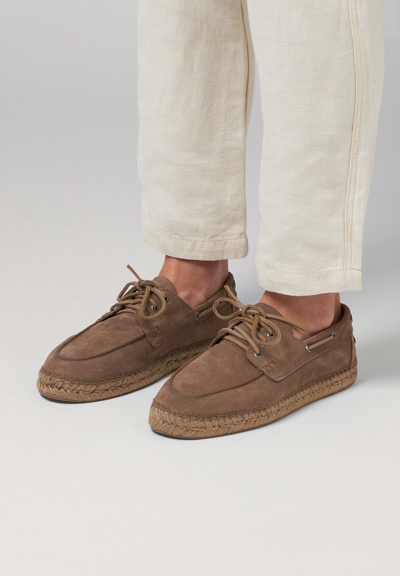 Brown suede shoes with a round toe, lace-up design, and woven jute sole. Features metal accents and a smooth texture.