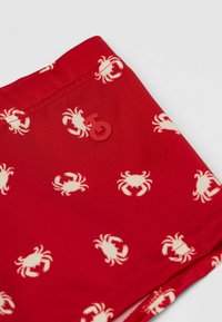 Røde svømshorts med et gentaget krabbe-mønster i cremefarve. Inkluderer en lille rød logo-detalje. Lavet af et glat, let materiale.