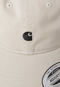 Beige caps med teksturert stoff, som har en svart brodert logo. Inkluderer et hvitt justeringstags på skjermen.