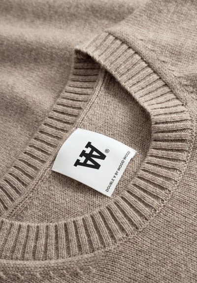 Pull tricoté beige à col rond, avec poignets et ourlet côtelés. Porte une étiquette de marque cousue dans l'encolure. Texture lisse.