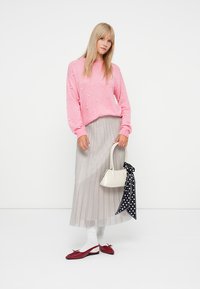 Rosa Pullover mit Perlendetails, silberner Faltenrock, weiße Handtasche, rote Ballerinas und ein schwarzes gepunktetes Tuch, das an der Tasche gebunden ist.