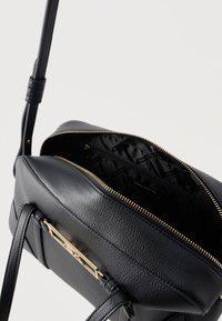 Μαύρο δερμάτινο τσάντα crossbody με χρυσό φερμουάρ και πλακέτα με το λογότυπο Armani Exchange, μερικώς ανοιχτή για να φαίνεται η εσωτερική επένδυση με την επωνυμία.