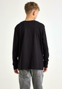 Sort langærmet skjorte med rund halsudskæring, lavet af bomuldsstof og i afslappet pasform, kombineret med grå denimjeans og set fra Bagside.