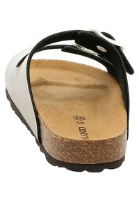 Sandal in bianco e nero con fondello in sughero, fasce in suede e decorazioni in metallo. Suola piatta con finitura texture.