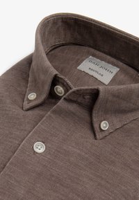 Camisa marrón de botones con una tela texturizada, que presenta un cuello extendido y botones blancos. La etiqueta dice "DAN JOHN REGULAR."