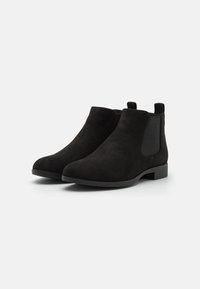 Black suede ankle boots with a smooth finish, elastic side panels, and a low stacked heel. Minimalist design with a rounded toe shape.