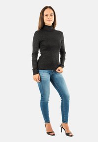 Maglione nero a collo alto con finitura testurizzata, abbinato a jeans skinny blu chiaro e sandali con tacco neri. Design semplice e aderente.