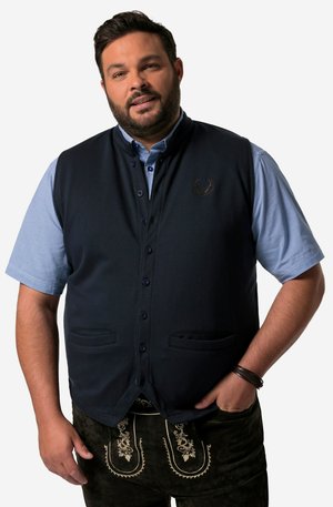 Chaleco sin mangas de color navy con una tela suave, botones frontales, dos bolsillos y un logotipo de asta bordado, combinado con una camisa de cuadro azul.