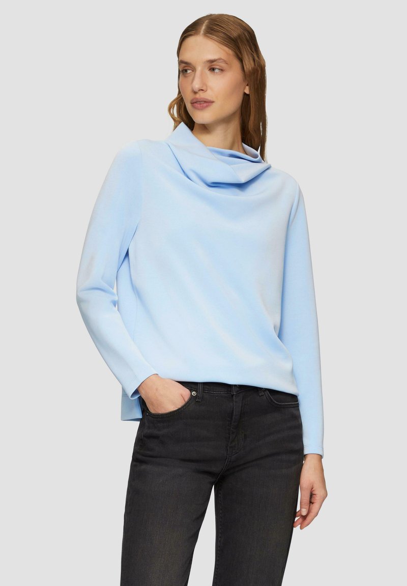 Lichtblauw lange mouwen top met een coltruik ontwerp, gemaakt van een zachte stof. Gecombineerd met donkere jeans, die een ontspannen pasvorm laten zien.