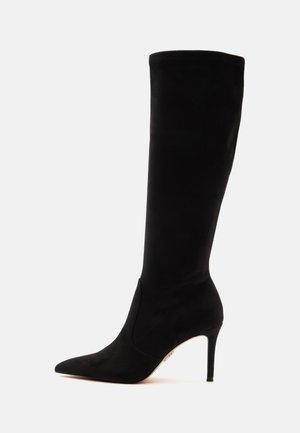 Botte haute en daim noir à bout pointu, talon aiguille fin et tige montant jusqu'au milieu du mollet.