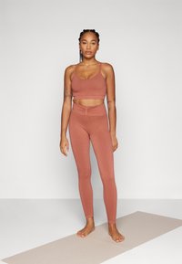 Sportssett i dempet terrakotta, med en kort topp og høyt liv leggings i teksturert stoff og tynne stropper.