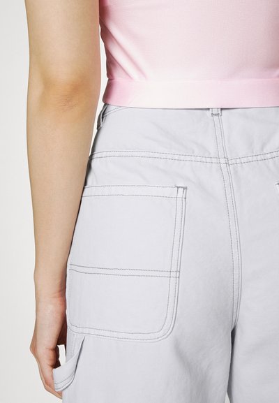 Ανοιχτό γκρι παντελόνια cargo με μεγάλες πλευρικές τσέπες, εμφανείς ραφές και άνετη εφαρμογή, σε συνδυασμό με ένα ροζ κοντό τοπ.