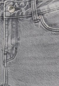 Gros plan sur un jean en denim gris montrant le bouton, la passants de ceinture, les poches et les détails de couture.