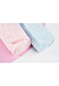 To håndklær rullet sammen i mykt, plysstoff. Det ene er lys rosa, det andre er lyseblått, hver med en tydelig knappedetalj.