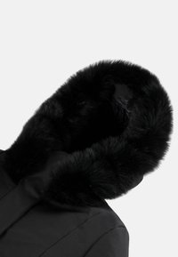 Parka nera con un ampio cappuccio rivestito in morbido pelo nero, tessuto elegante e superficie liscia. Il design enfatizza calore e comfort.