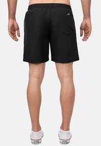 Pantaloni da bagno neri con vita elasticizzata, una tasca posteriore e una texture liscia, abbinati a sneakers bianche.