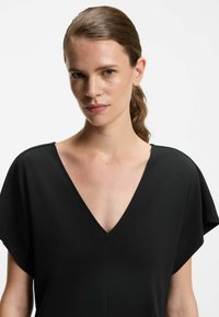 Top nero a scollatura a V con maniche corte e larghe. Realizzato in tessuto morbido, presenta un design minimalista e nessun motivo o accentuazione visibile.