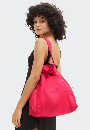 Röd nylon tote-väska med en dragsko upptill, med en cirkulär logotyp och breda axelremmar. Slät textur med en strukturerad form.