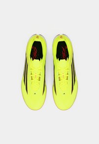 Φωτεινά κίτρινα ποδοσφαιρικά παπούτσια με μαύρες ρίγες, σχέδιο με κορδόνια, υφή στην επάνω επιφάνεια και αντίθετες κόκκινες λεπτομέρειες στο λογότυπο της μάρκας και το όνομα του μοντέλου.