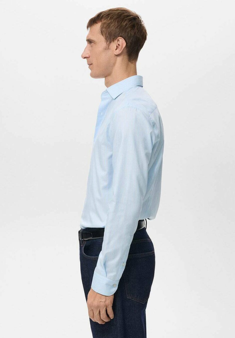 Hellblau gestreiftes Hemd mit Knopfkragen, langen Ärmeln und figurbetontem Design, getragen mit dunklen Jeans und einem schwarzen Gürtel.