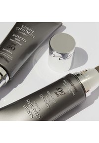 Graue Röhrchen mit Sonnencreme, beschriftet mit "Sarah Chapman Skinisiss", mit SPF 50, versehen mit silbernen Kappen und einem eleganten, modernen Design.