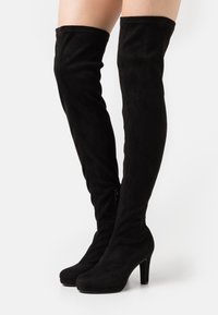 Botas negras por encima de la rodilla hechas de suave ante, con puntera redondeada, tacón alto y cremallera lateral para el cierre.