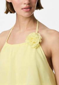 Top giallo a fascia realizzato in tessuto leggero, con un accento floreale sulla spalla e un collo arricciato per una maggiore texture.