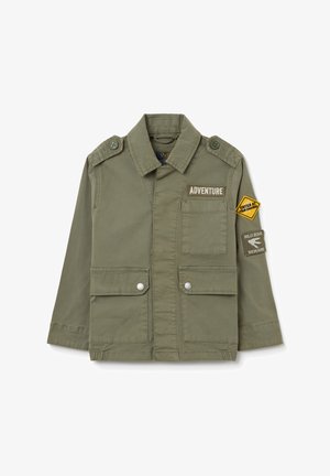 Olivgrüne Jacke mit Kragen, Fronttaschen und gesteppter Schulterklappen. Mit Patches: "ABENTEUER!" und Warn-Dreieck.