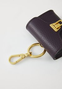 Portafoglio portachiavi in pelle textured viola con chiusura in oro, dotato di un anello metallico e dettaglio di logo in rilievo. Design compatto e funzionale.