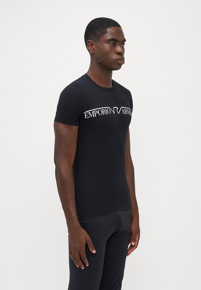 Melns īsām piedurknēm T-krekls, kas izgatavots no mīksta kokvilnas; uz krūtīm ir izteikta baltā Emporio Armani logo. Šaurs piegriezums.
