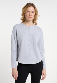 Světle šedá mikina s kulatým výstřihem, předním zapínáním na knoflíky, dlouhými rukávy a jednou kapsou na hrudi. Hladká textura a volný střih.