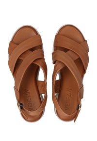 Bruine leren sandalen met gekruiste banden, een open achterkant en een lage, platte witte zool. Opvallend logo zichtbaar op het voetbed.