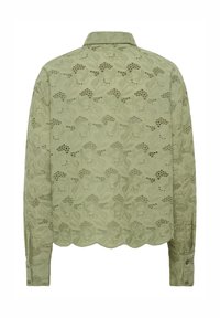 Chemisier en dentelle verte avec un motif floral, ourlet festonné, manches boutonnées et col classique. La vue de dos met en avant une texture complexe.
