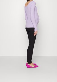 Camiseta de manga larga de lavanda con textura acanalada y escote en la espalda, combinada con jeans ajustados negros y zapatos planos de ante rosa brillante.