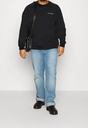 Sweat-shirt noir avec des poignets et un ourlet côtelés, logo avant en bleu clair, associé à un jean bleu clair et des chaussures en cuir noires. Sac bandoulière inclus.