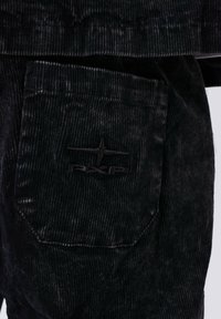 Tessuto a coste nero con un pattern verticale testurizzato e un logo a stella ricamato sopra le lettere "FXP" su una tasca.