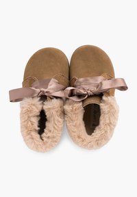 Zapatillas de ante marrón con suave forro de piel sintética beige y un lazo decorativo de satén en la parte delantera. Suelas planas y redondeadas completan el diseño.