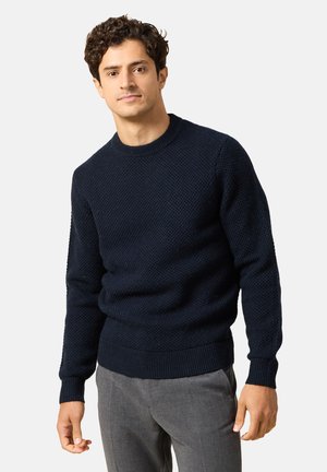 Dunkelblauer Strickpullover mit strukturiertem Muster, Rundhalsausschnitt, gerippten Bündchen und Saum, kombiniert mit grauen Hosen.