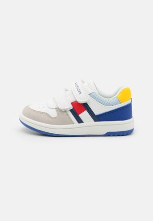 Sneaker bianco con accenti grigi, blu e rossi. Presenta una texture liscia, due cinturini in Velcro e una suola in gomma blu.