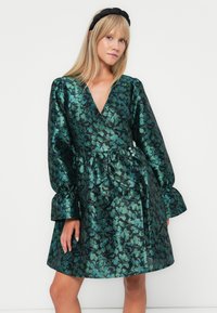 Green and blue floral pattern wrap dress with long, puffed sleeves, cinched waist, and flared skirt; made from a shiny, textured fabric.