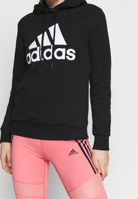 Felpa nera in pile con logo stampato bianco e coulisse. Abbinata a leggings rosa con strisce nere e dettagli del logo.
