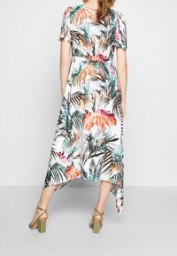 Klänning med blommönster, korta ärmar, markerad midja och ojämn fåll. Färgerna inkluderar grönt, orange och rosa på vit bakgrund.