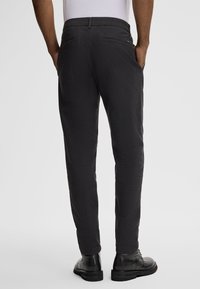 Black textured trousers with tapered legs, side pockets, and decorative stitching, paired with black footwear.