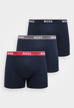 Trois boxers pour hommes en marine avec ceintures élastiques en rouge, gris et noir, chacun marqué du logo "BOSS" en couleurs contrastantes.