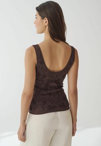 Bruine gebreide tanktop met een bloemenprint en brede schouderbanden. Heeft een ronde rugontwerp en is gecombineerd met lichtgekleurde, loszittende broeken.