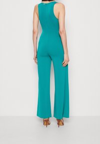 Mono turquesa con un cuerpo ajustado y piernas acampanadas, con cremallera en la parte posterior y diseño sin mangas. Textura suave y color sólido.