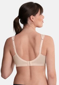 Beżowy biustonosz z regulowanymi ramiączkami, bezszwowym wzorem i niskim tyłem. Posiada zapięcie na haczyk i oczko oraz miękką, gładką teksturę materiału.
