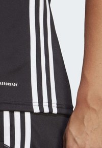 Černé sportovní tričko se bílými pruhy po stranách a textem "AEROREADY". Materiál vypadá hladce, navržený pro výkon.