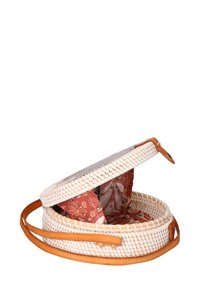 Cesto rotondo intrecciato con esterno bianco e fodera in tessuto a motivo rosso. Presenta una tracolla in pelle e una chiusura a tappo.