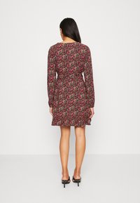 Schwarzes Kleid mit einem floralen Muster aus pinken, grünen und gelben Blumen. Lange Ärmel, tailliert und mit einem ausgestellten Rock, der über dem Knie endet.